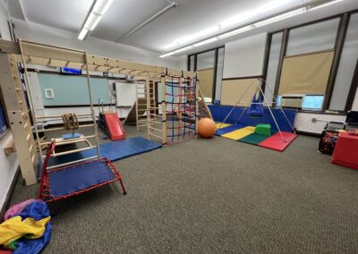 Side view of a Sensory Integration Room with a wooden climbing structure and colorful swings, slides, beanbags and ball pit.