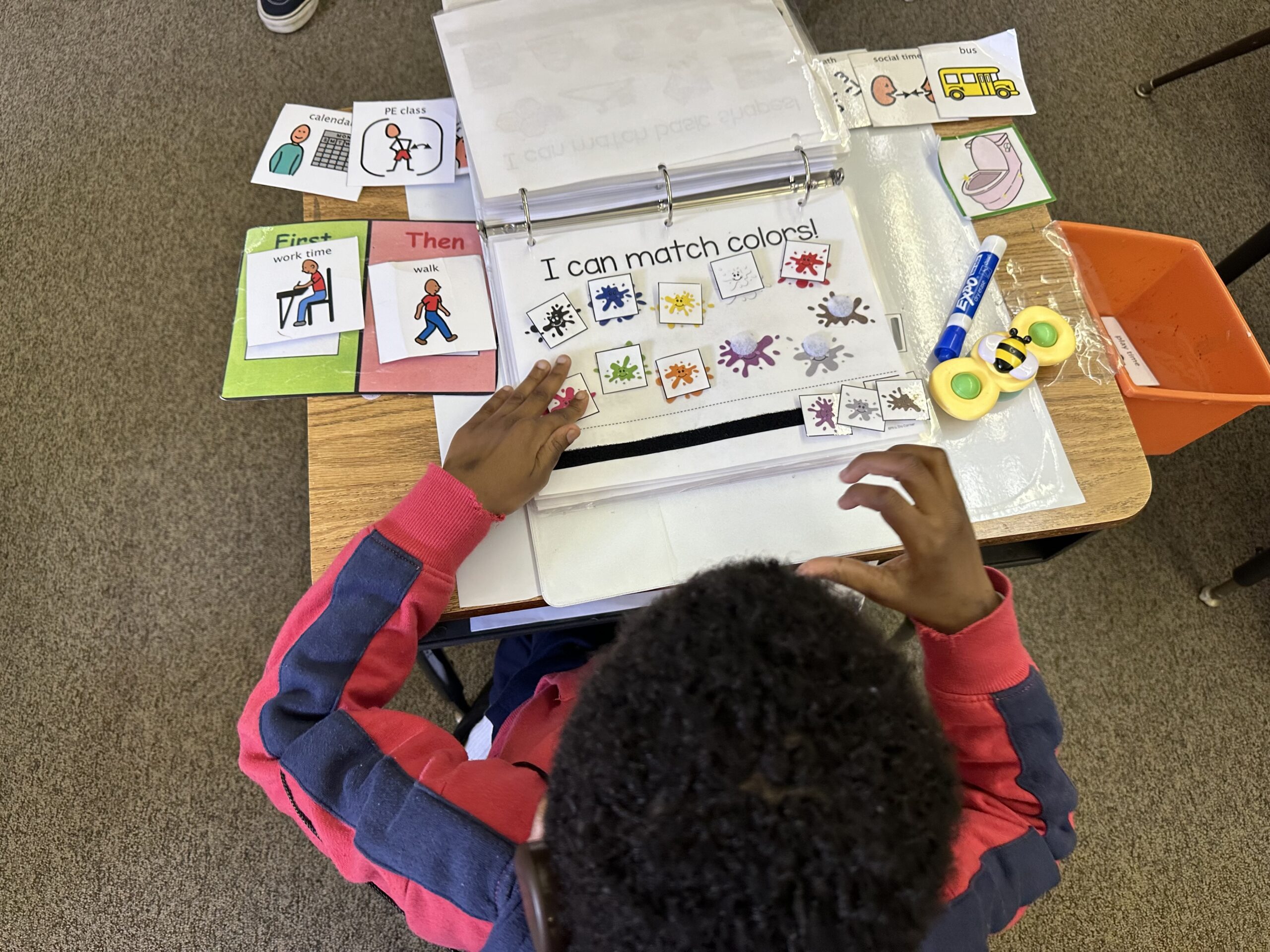 A student is working on matching colors independently. He has a First, Then and Visual Schedule on his desk for support.