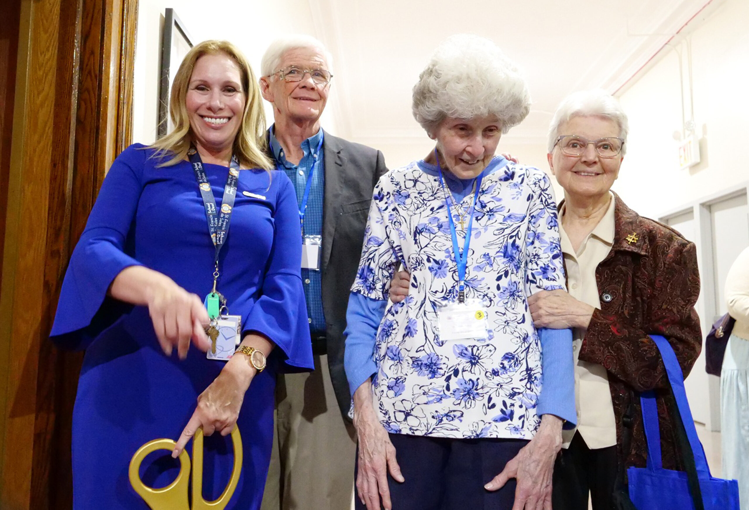 Dr. Jodi Falk holding oversized gold scissors at the ribbon cutting for the Deaf and DeafBlind Museum and Research Center, standing with guests including New York State Assembly members.