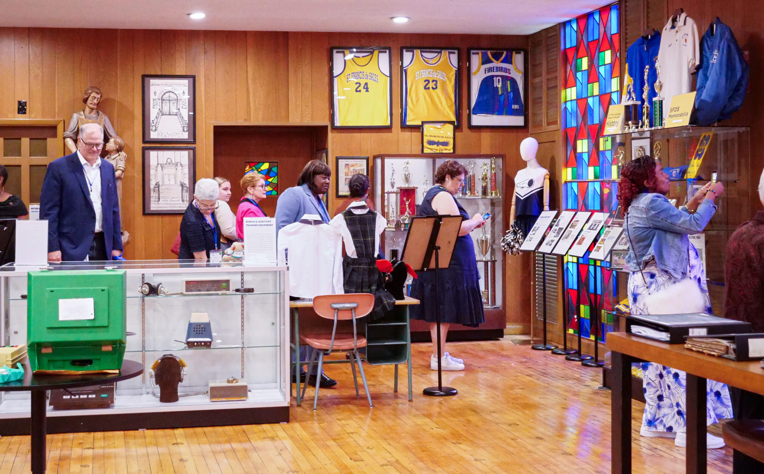 Visitors walking through the Deaf and DeafBlind Museum and Research Center, a wood panelled gallery lined with glass display cases and framed exhibits.