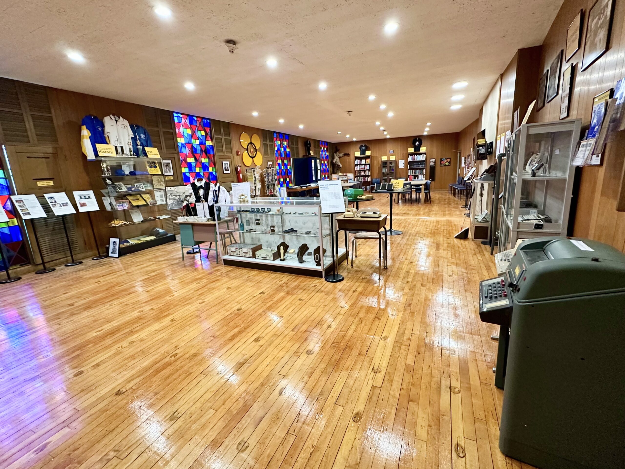 Interior of the Deaf and DeafBlind Museum, a wood panelled room with glass display cases along the walls and a polished wooden floor.