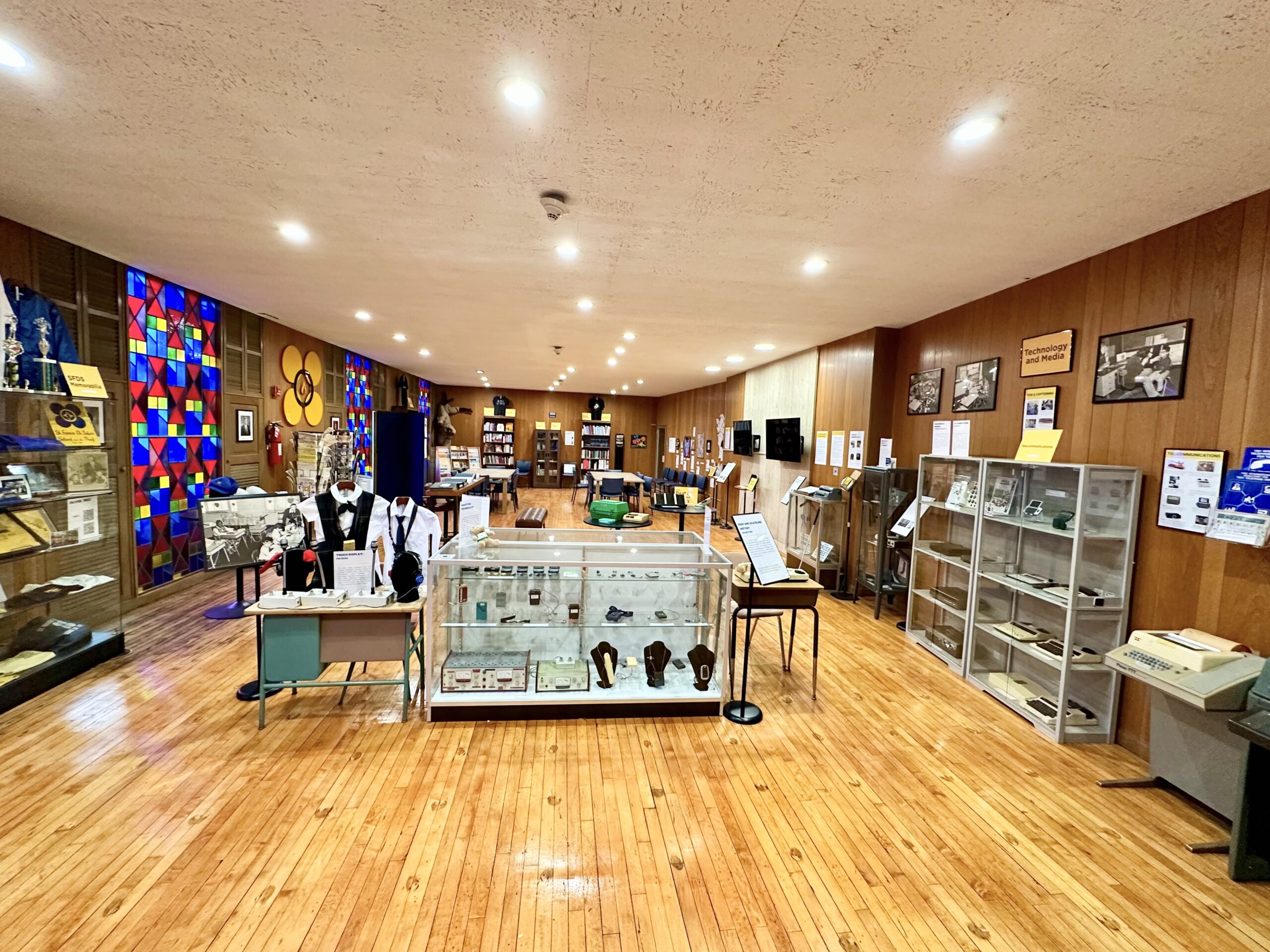 Museum gallery lined with tall display cases holding historical objects and photographs from the school's history.