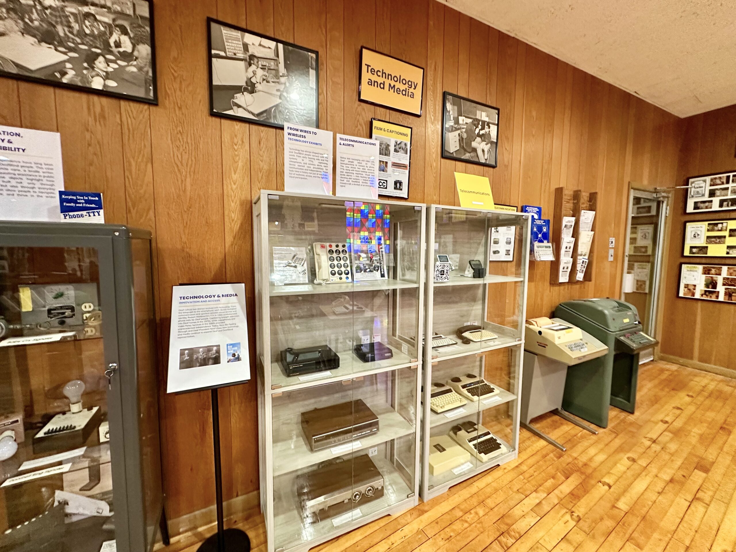 Museum display cabinets holding artefacts, with framed documents and photographs mounted on the wall behind them.