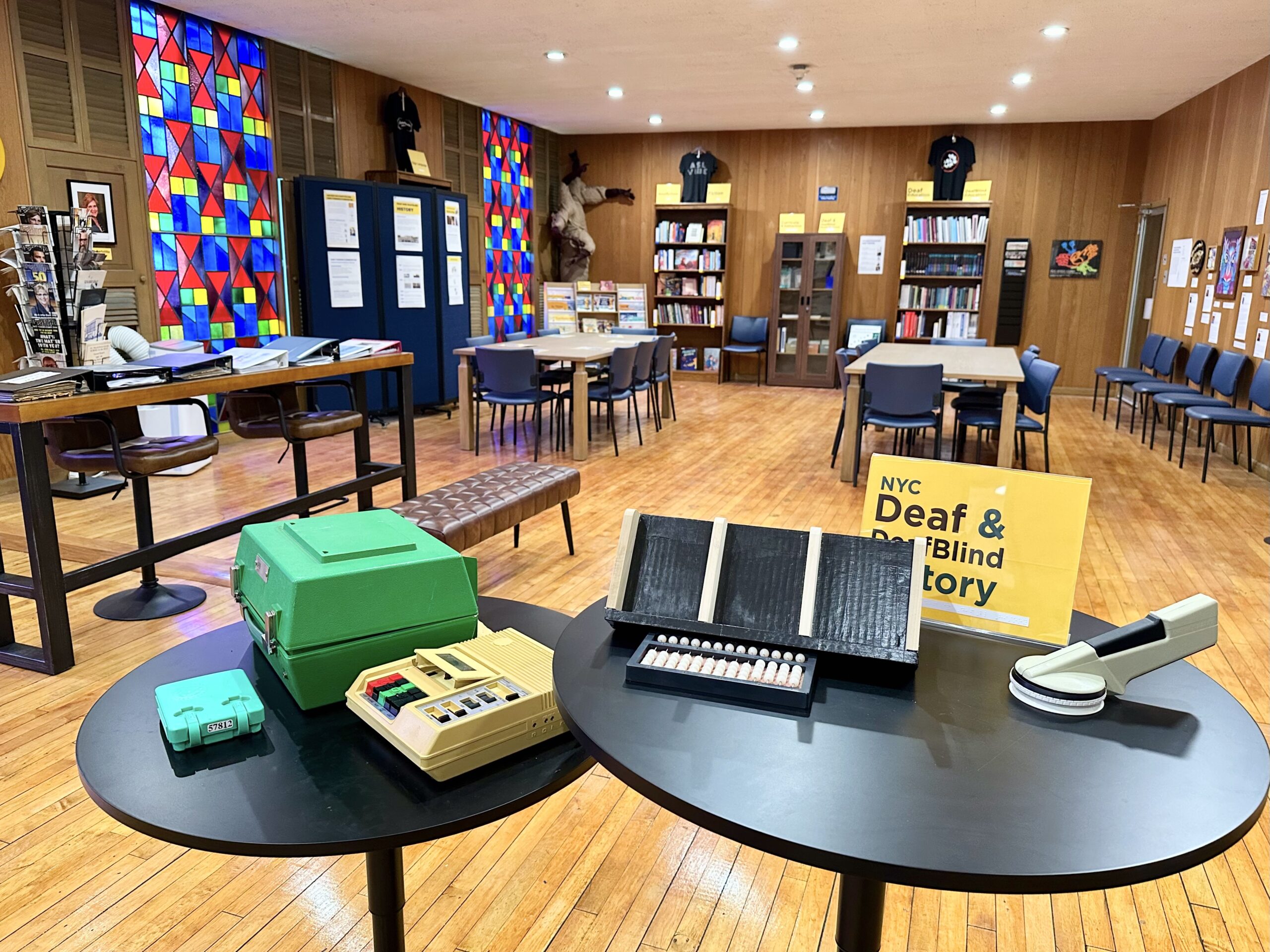 Round table in the museum holding historical communication equipment, including a teletypewriter, beside a Deaf and Blind History display sign.