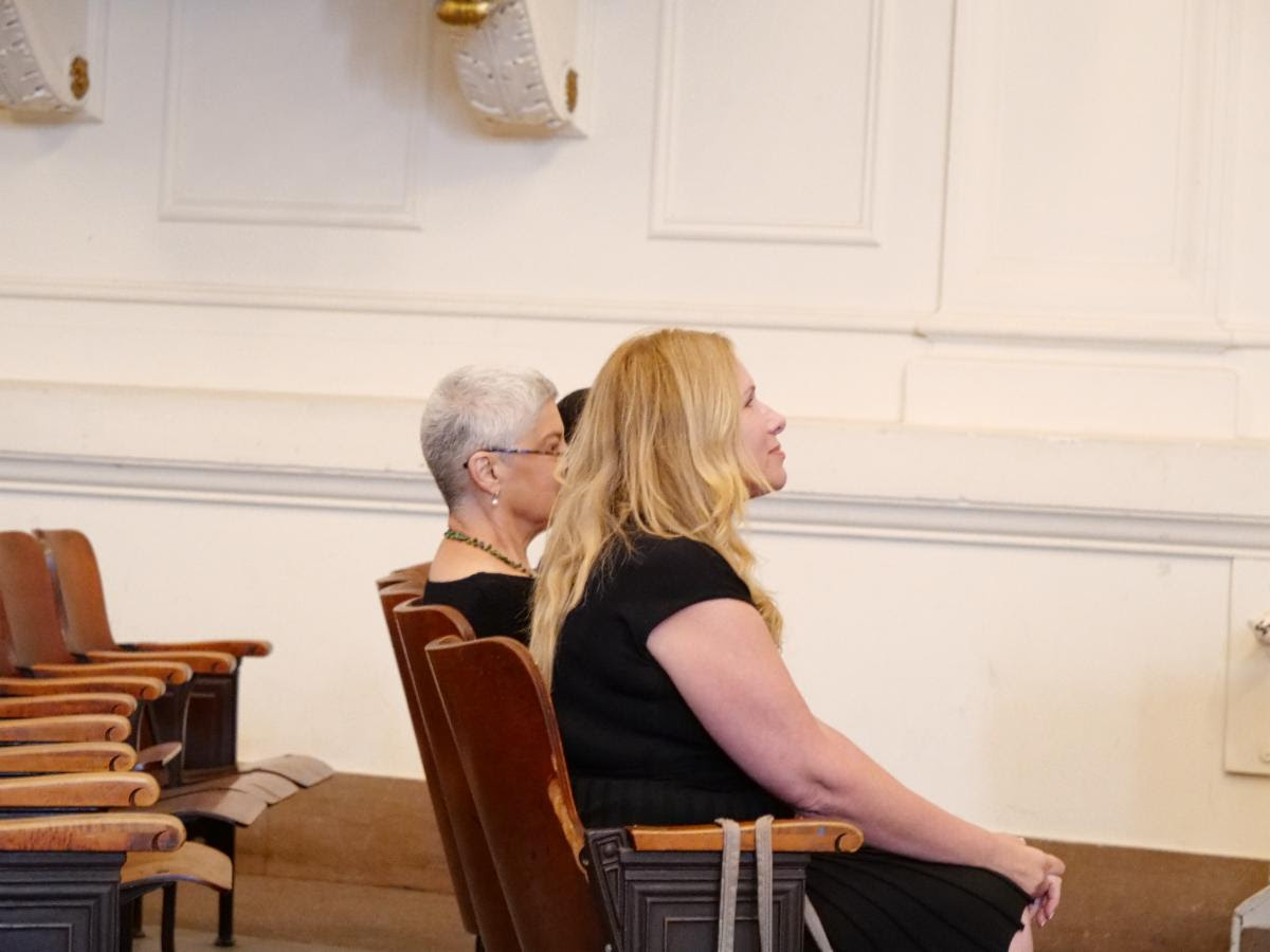 Two people seated together in conversation, one signing to the other.