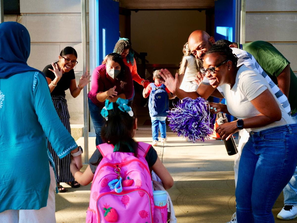 Staff and families greeting one another at the school's accessible entrance beneath the blue awning.