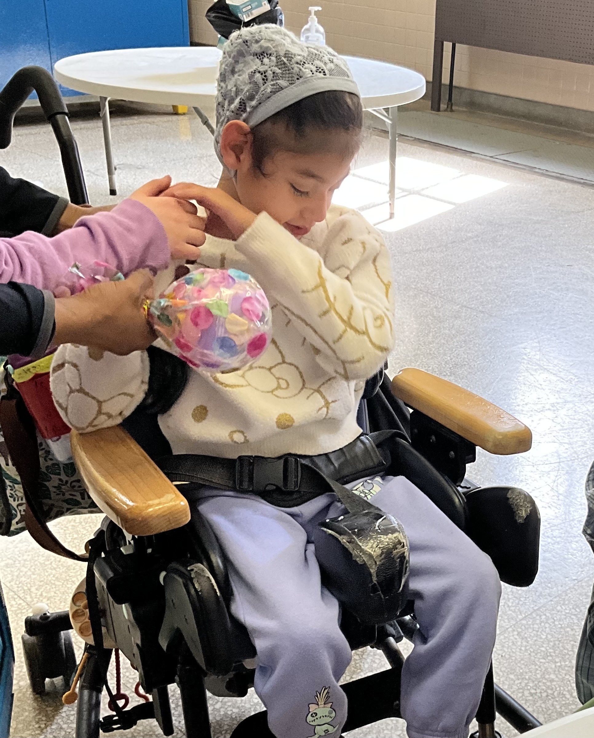 A young student in a wheelchair explores a colorful sensory ball held by a caregiver during Empowerment Saturday.