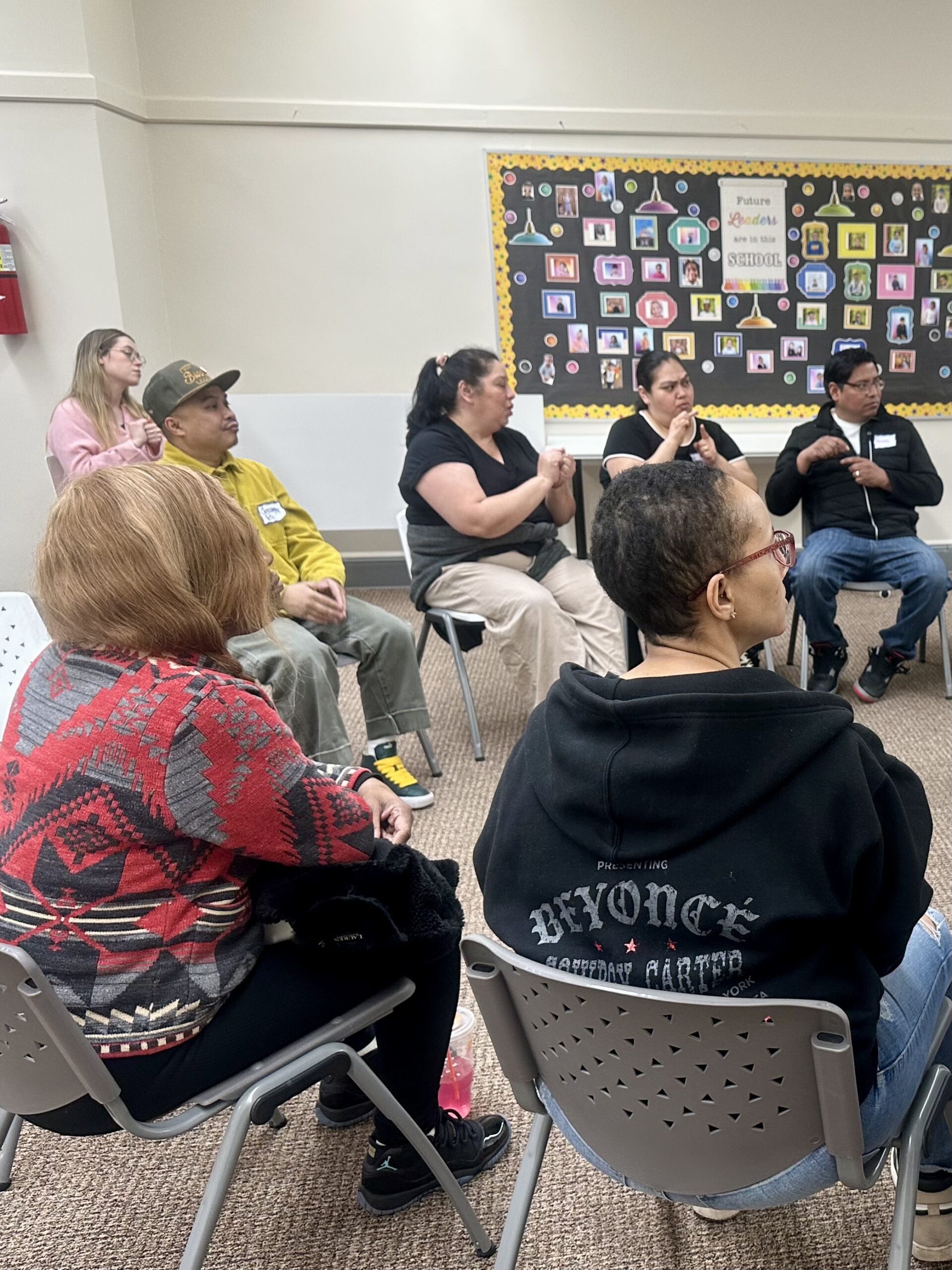 A family support group sits in a circle, parents and caregivers signing to one another.