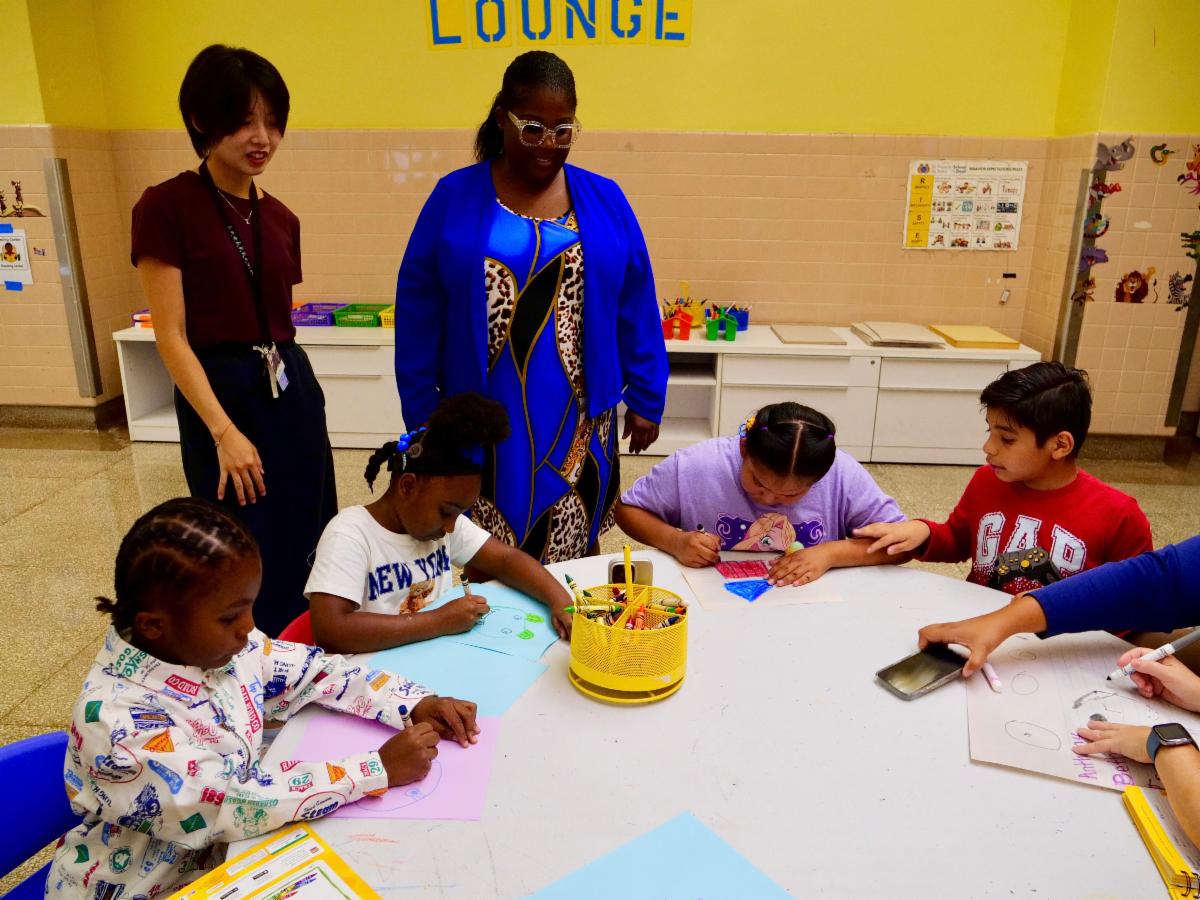 Students drawing together around a table in the Literacy Lounge while two staff members look on.